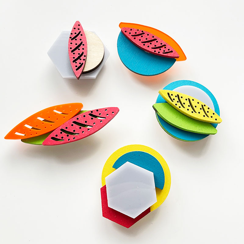 Five brooches made from brightly coloured plastic sit on a white surface.